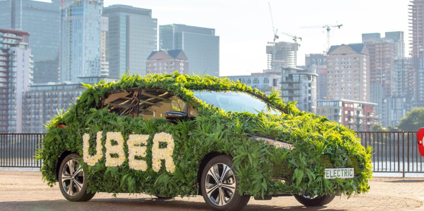 A Sedan covered in plants with flowers spelling the word "UBER"