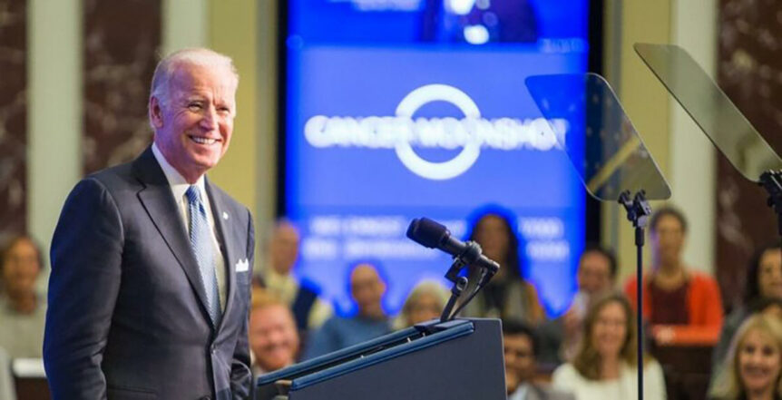 President Biden wearing a suit and standing at a podium in front of a crowd of people