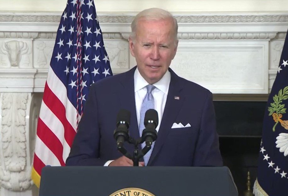 President Biden wearing a navy blue suit standing behind a podium.
