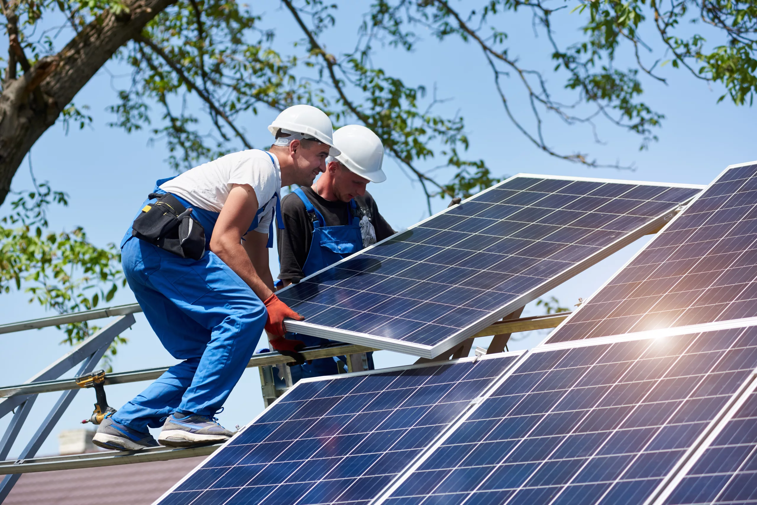 Two young technicians installing heavy solar photo voltaic panels on a multifamily property.